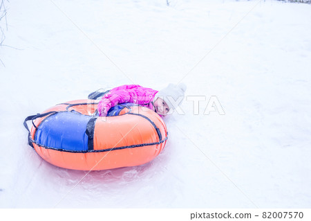 A cheerful girl in warm clothes rides down snowy hill on slide-slide cheesecake A cheerful girl in warm clothes rides down snowy hill on slide-slide cheesecake 82007570