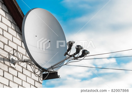 Satellite dish on a white brick wall of a house against a blue sky with clouds Satellite dish on a white brick wall of a house against a blue sky with clouds 82007866