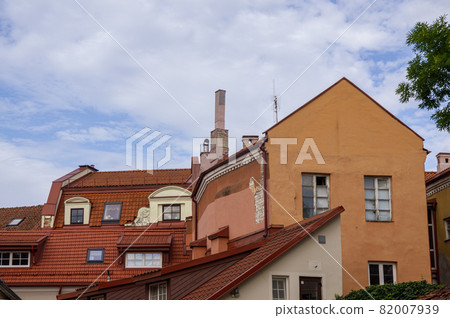 Abstract conceptual architecture of vintage roofs of houses with windows, balconies and oven and ventilation pipes against blue sky with clouds in old Town. Apartments in the attic against skyline Abstract conceptual architecture of vintage roofs of houses with windows, balconies and oven and ventilation pipes against blue sky with clouds in old Town. Apartments in the attic against skyline 82007939