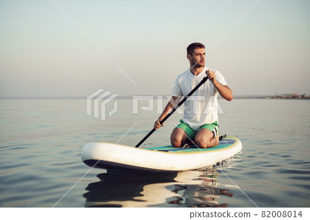 Young man in t-shirt and shorts floating on SUP board Young man in t-shirt and shorts floating on SUP board 82008014