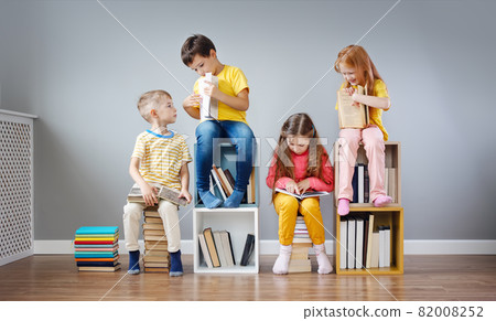 Group of children sitting on the book's stacks and on the bookshelves in the room and reading periodical. 82008252