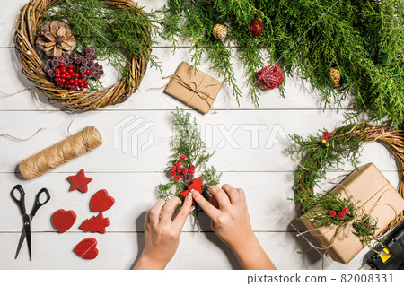Christmas handmade diy background. Making craft xmas wreath and ornaments. Top view of white wooden table with female hands. 82008331