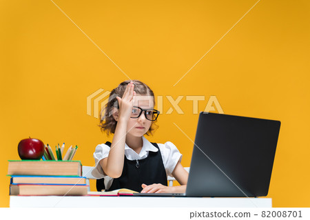 Schoolgirl in glasses raising hand sitting at laptop during online lesson. Distant School Learning. Schoolgirl in glasses raising hand sitting at laptop during online lesson. Distant School Learning. 82008701