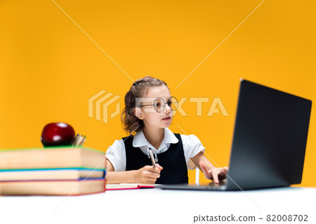 Schoolgirl in glasses writing and looking at laptop during online lesson. Distant School Learning. 82008702