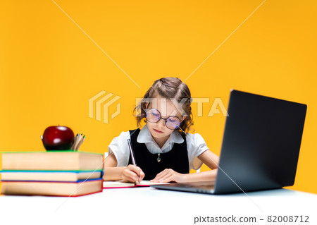 Schoolgirl in glasses writing and sitting at laptop during online lesson. Distant School Learning. Schoolgirl in glasses writing and sitting at laptop during online lesson. Distant School Learning. 82008712