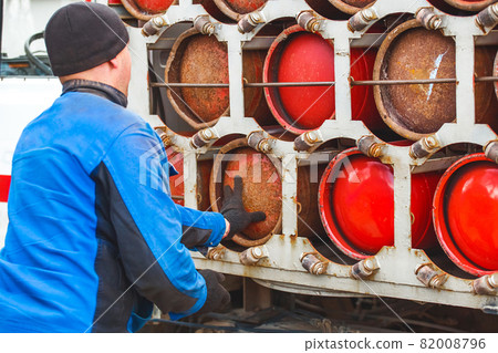 Male industrial worker puts a gas cylinder into a gas machine. Equipment for the safe transportation of propane gas bottles Male industrial worker puts a gas cylinder into a gas machine. Equipment for the safe transportation of propane gas bottles 82008796