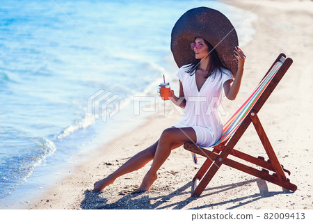 Pretty woman in big straw hat relaxing on a lounger beach and drinks refreshing juice. summer vacation concept Pretty woman in big straw hat relaxing on a lounger beach and drinks refreshing juice. summer vacation concept 82009413