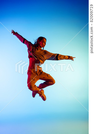 One young sportive girl dancing hip-hop in stylish clothes on colorful background at dance hall in neon light. Youth culture, movement, style and fashion, action. 82009719