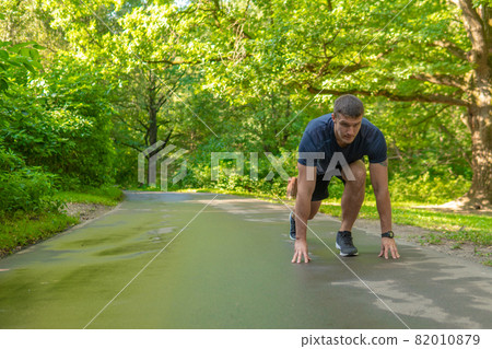 A man athlete runs in the park outdoors, around the forest, oak trees green grass young enduring athletic athlete active runner nature, training wellness park leisure spring, morning stretches 82010879