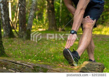 A young enduring athletic athlete is doing stretching in the forest outdoors, around the forest, oak trees. runner lifestyle jogger fit person marathon, park wellbeing. Summer running, feet stretches 82010881