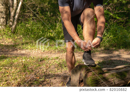 The sportsman is tying the laces of his legs in sneakers close up the athlete runs in the park outdoors, around the forest, oak trees green grass young enduring athletic athlete run athlete fitness The sportsman is tying the laces of his legs in sneakers close up the athlete runs in the park outdoors, around the forest, oak trees green grass young enduring athletic athlete run athlete fitness 82010882