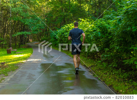 A man athlete runs in the park outdoors, around the forest, oak trees green grass young enduring athletic athlete runner lifestyle outdoor athletic motion, jogging outside. Autumn leisure morning 82010883