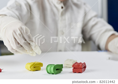 Cropped shot of kid hands in protective latex gloves making plasticine figures on the table Cropped shot of kid hands in protective latex gloves making plasticine figures on the table 82011442