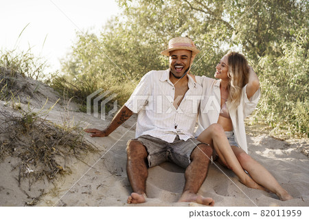 Young couple sitting next to each other on beach Young couple sitting next to each other on beach 82011959