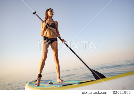 Young attractive woman standing on paddle board 82011963