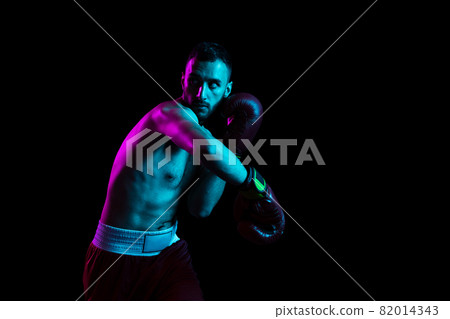 One professional male boxer training isolated over black backgrund in neon light. Knocking out the opponent One professional male boxer training isolated over black backgrund in neon light. Knocking out the opponent 82014343