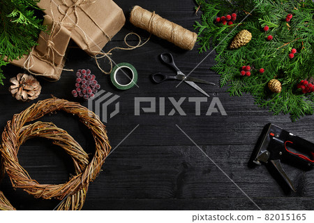 Make a Christmas wreath with your own hands. Spruce branch, Christmas wreath and gifts on a black wooden background Make a Christmas wreath with your own hands. Spruce branch, Christmas wreath and gifts on a black wooden background 82015165