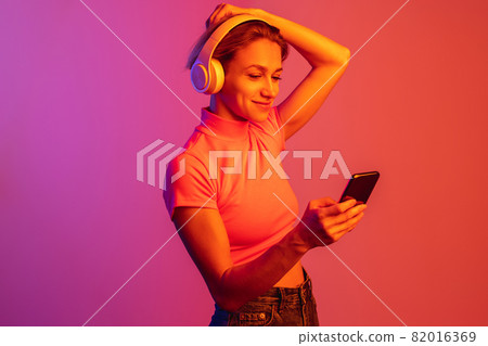 One caucasian girl in headphones putting hair up isolated over gradient background in neon lights One caucasian girl in headphones putting hair up isolated over gradient background in neon lights 82016369