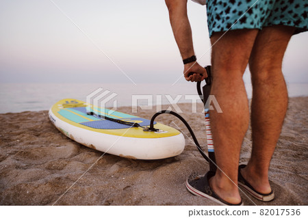 Close up of man prepares to paddle surf on a beach inflating sup board 82017536
