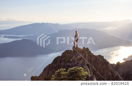 Adventurous Caucasian Woman Hiking on top of a Rocky Mountain Cliff. Adventurous Caucasian Woman Hiking on top of a Rocky Mountain Cliff. 82019428