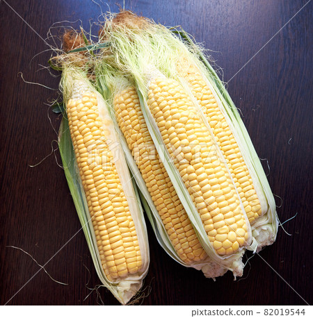 Four golden ears of corn with leaves. Low key. Top view 82019544