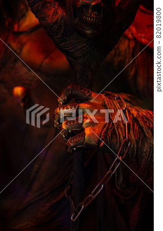 Halloween decorations, spooky creepy scary fearfull horrible terrible warlock's hand in rags with metal fingers and a chain holding frighten skull mask in bloody red orange gold colors 82019800