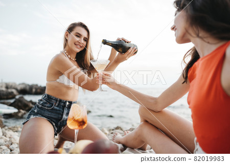 Two young female friends having picnic on a beach drinking cocktails Two young female friends having picnic on a beach drinking cocktails 82019983