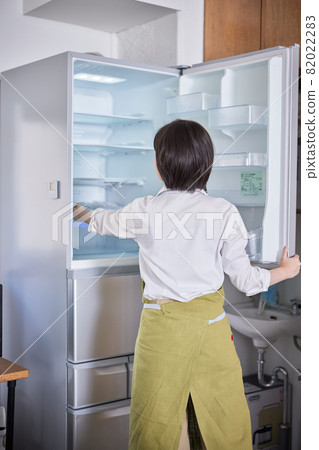 A young woman in an apron taking out ingredients from the refrigerator A young woman in an apron taking out ingredients from the refrigerator 82022283