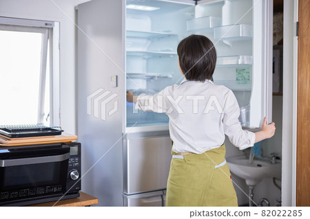 A young woman in an apron taking out ingredients from the refrigerator 82022285