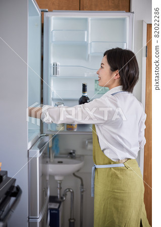A young woman in an apron taking out ingredients from the refrigerator A young woman in an apron taking out ingredients from the refrigerator 82022286