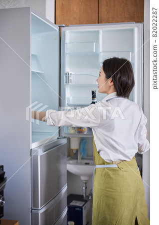 一個穿著圍裙的年輕女子從冰箱裡取出食材 一個穿著圍裙的年輕女子從冰箱裡取出食材 82022287