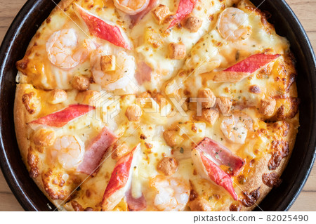 Close up of delicious seafood pizza topped with cheese, pineapple, crab sticks and shrimp on wooden table. Pizza is a favorite food for many around the world. 82025490