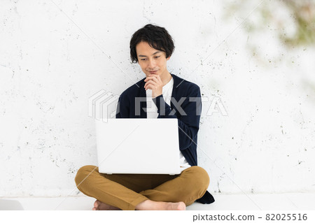 一個年輕人坐在地板上,在電腦上工作 一個年輕人坐在地板上,在電腦上工作 82025516