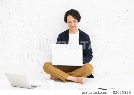 一個年輕人坐在地板上，在電腦上工作 82025529