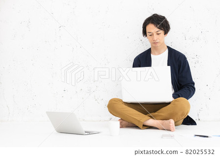 A young man sitting on the floor and working on a computer A young man sitting on the floor and working on a computer 82025532