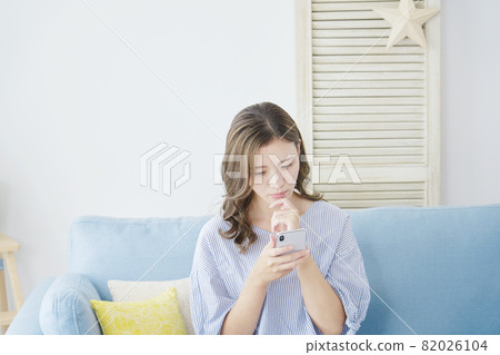 A woman thinking with a smartphone in the room A woman thinking with a smartphone in the room 82026104