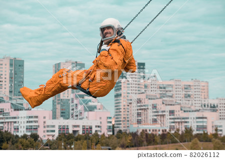Happy astronaut smiling and looking at camera while swinging on swing outdoors. Happy astronaut smiling and looking at camera while swinging on swing outdoors. 82026112