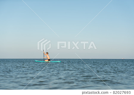 A 12 year old boy learns to stand on a SUP board in the sea near the shore. A 12 year old boy learns to stand on a SUP board in the sea near the shore. 82027693