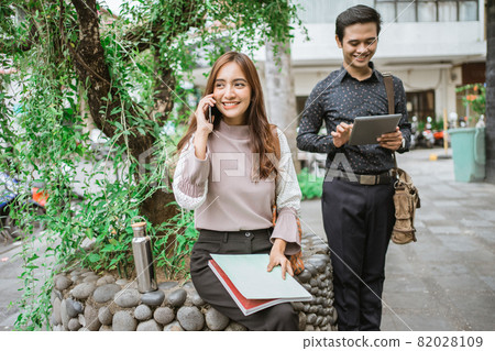 two busy worker sitting in the park during office break using phone 82028109