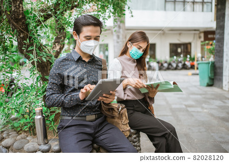 man and woman sitting on the park bench with tablet 82028120