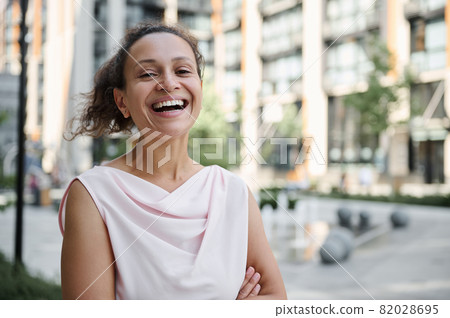 Attractive mixed race Hispanic, African American woman smiling with toothy smile standing on the urban buildings background. Confident portrait of a beautiful business woman Attractive mixed race Hispanic, African American woman smiling with toothy smile standing on the urban buildings background. Confident portrait of a beautiful business woman 82028695