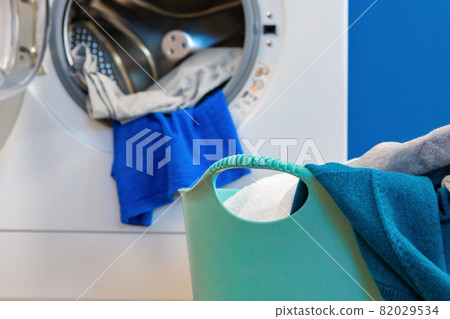 Washing machine with laundry on blue wall background Washing machine with laundry on blue wall background 82029534
