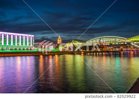 View of the colorful Bogdan Khmelnitsky bridge illuminated at night reflecting in the Moskova river. Moscow Kiyevsky railway station at night. Moscow, Russia View of the colorful Bogdan Khmelnitsky bridge illuminated at night reflecting in the Moskova river. Moscow Kiyevsky railway station at night. Moscow, Russia 82029922