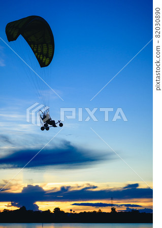 A Silhouette paramotor pilot flying over a lake with the sunset sky background 82030890