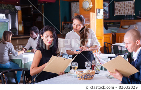 positive female busboy taking order to couple in modern restaurante 82032029