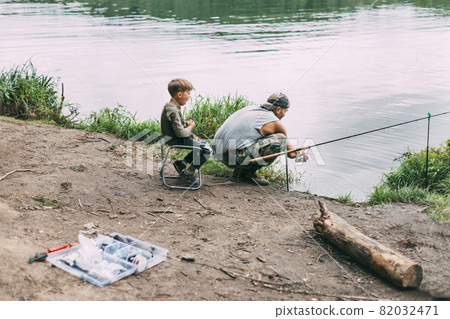 A young man teaches his children to fish during a family vacation at a camping site. Hobbies, vacations, weekends, fishing 82032471
