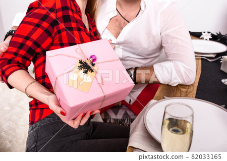 Picture showing group of friends celebrating Christmas at home and giving presents to each other. Focus on a gift in woman hands in the foreground Picture showing group of friends celebrating Christmas at home and giving presents to each other. Focus on a gift in woman hands in the foreground 82033165