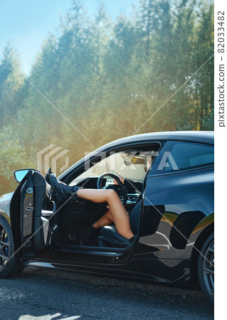 Young woman parked on the side of the road, opened the door and put her foot on her Young woman parked on the side of the road, opened the door and put her foot on her 82033482