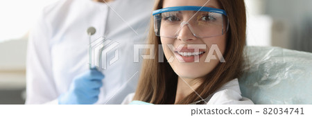 Woman patient in safety glasses sitting in dental chair near doctor 82034741