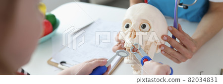 Little girl pulling out tooth from artificial skull with children dental instruments closeup 82034831